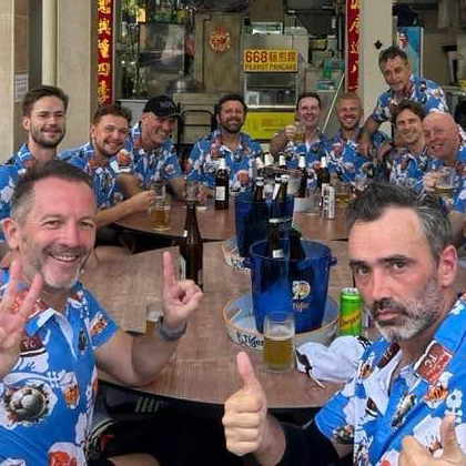 CBD Wanderers squad round a table of beers in matching blue hibiscus print shirts