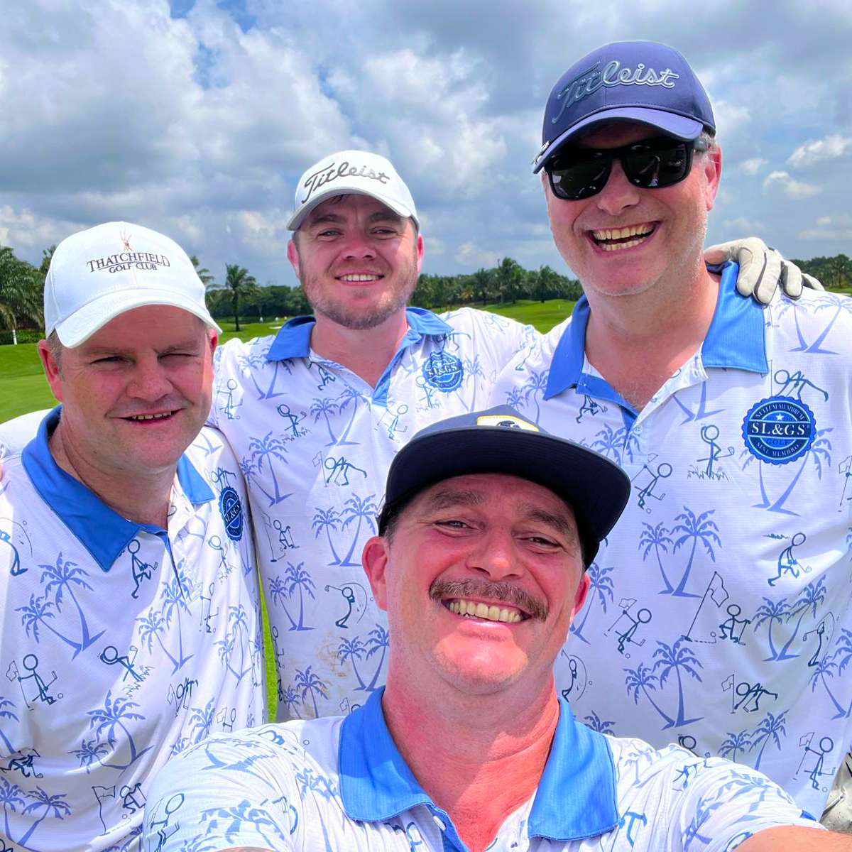 Four SL&GS golfers grinning on a Vietnam fairway in matching white and blue palm-print tour polos