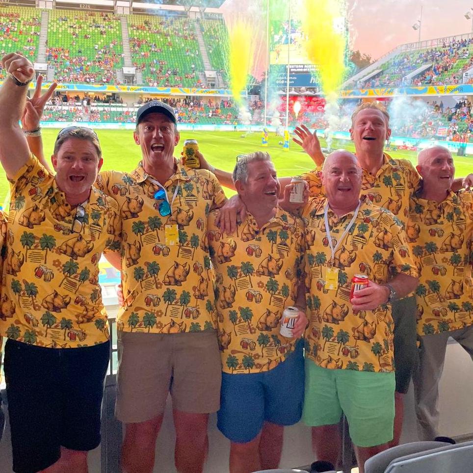 Rhinos RFC members in matching yellow Hawaiian tour polos at a rugby sevens stadium