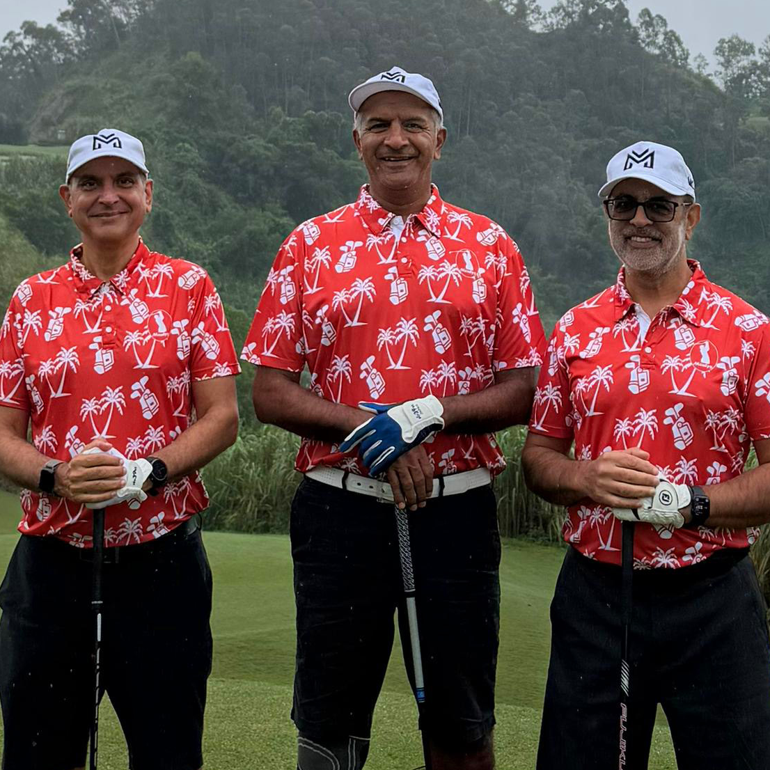 Three Monty's golfers in matching red palm-print tour polos and caps on a misty Vietnam course